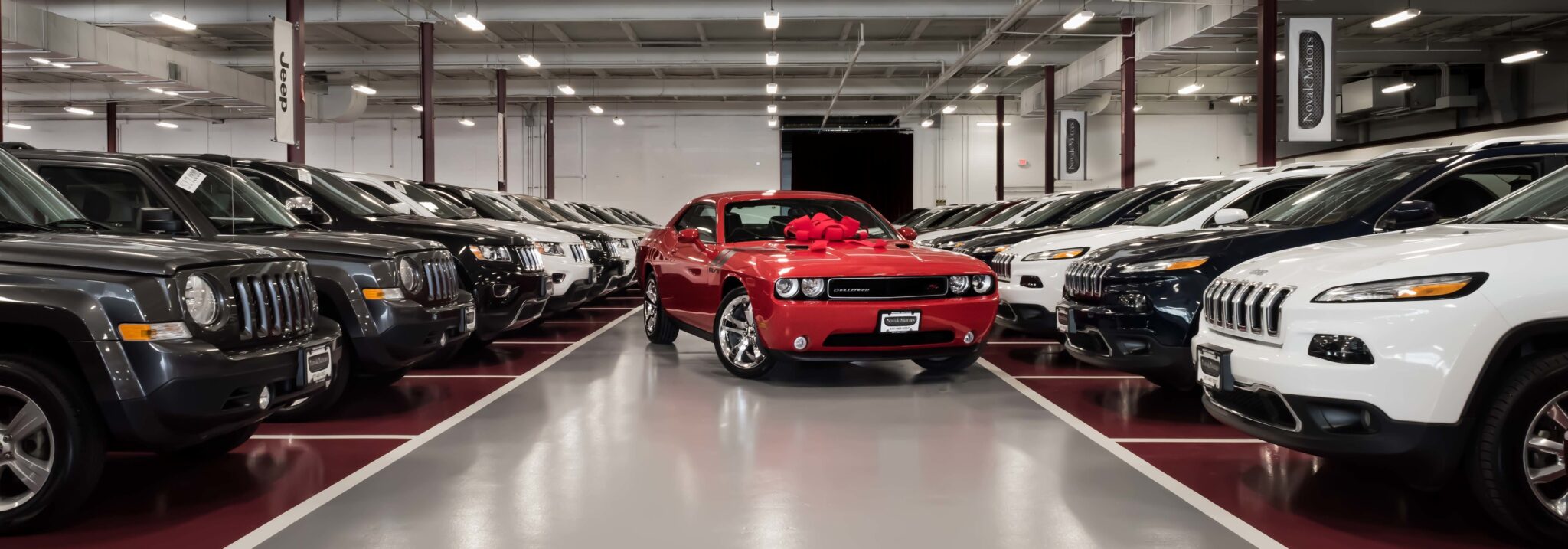 Rows of vehicles inside a Novak Motors showroom with a red Dodge Challenger centered in front, symbolizing CU Xpress Lease’s growth to over 195,000 leased vehicles and $7.4 billion in lending by 2025.